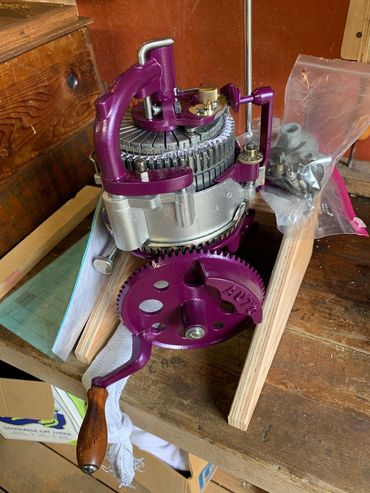 Vintage purple hand-crank knitting machine on a wooden table.