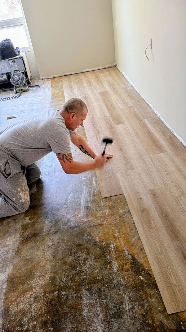 Man installing wood laminate flooring with a mallet indoors.