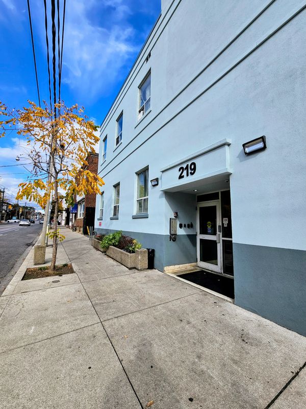 Urban street view with a light blue building numbered 219 and autumn foliage on a sunny day.