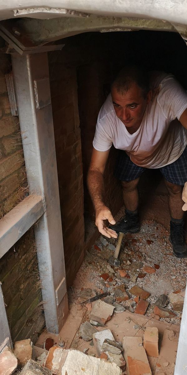 Man working in a narrow brick-lined underground space with rubble.
