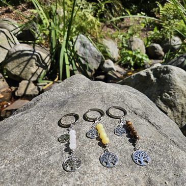 Three beaded keychains with tree charms on a large rock in nature.