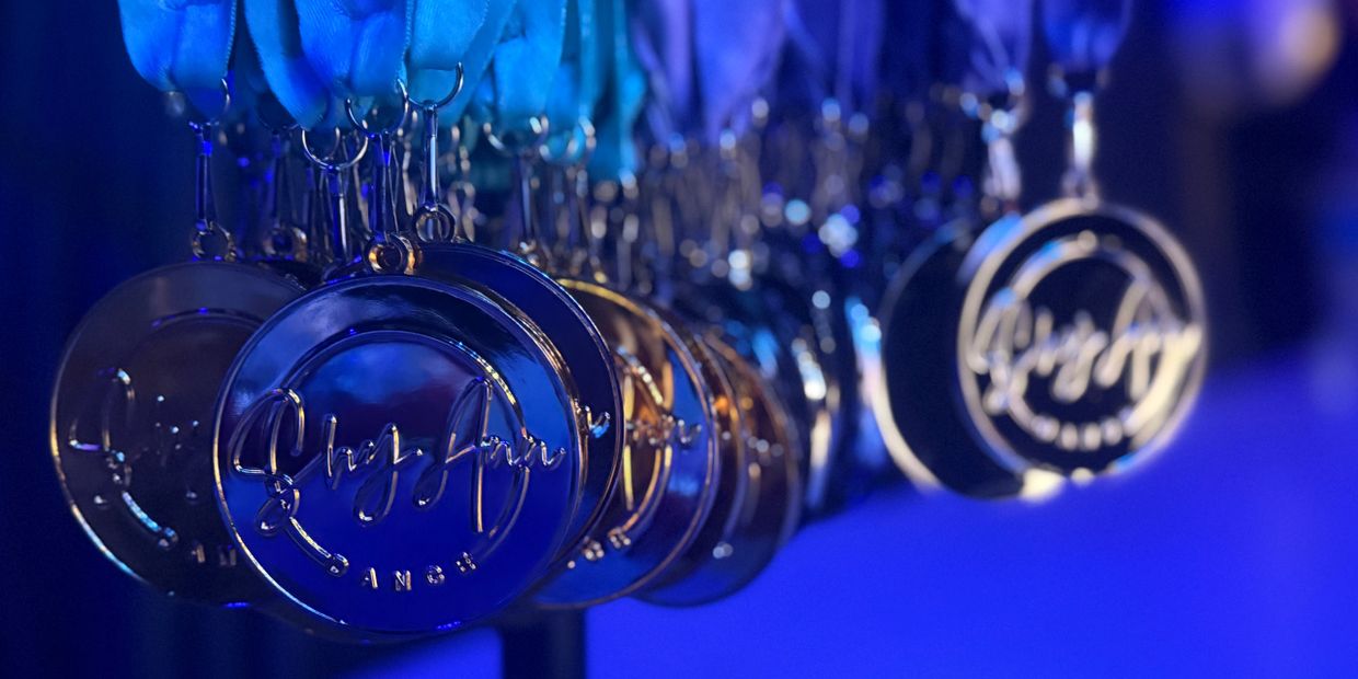 Close-up of shiny medals hanging on blue ribbons under blue lighting.