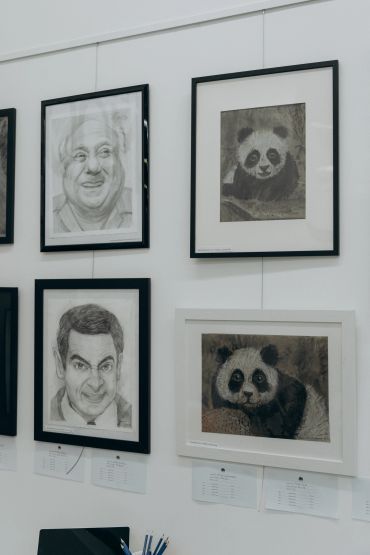 Framed pencil sketches of two men and two pandas on a white wall.