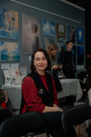 Woman sitting in an art gallery with paintings behind her.