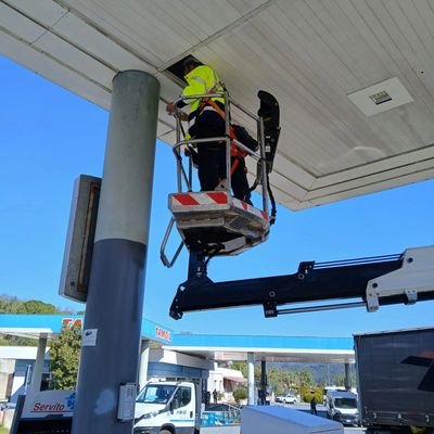 Worker in safety gear repairing a light fixture at a gas station.