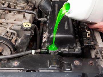 Pouring green coolant into a car engine.