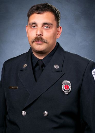 A firefighter in formal uniform with badges and a mustache poses for a portrait.