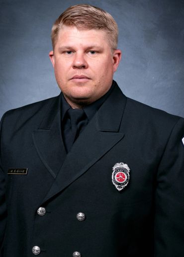 Portrait of a serious firefighter in uniform against a plain background.