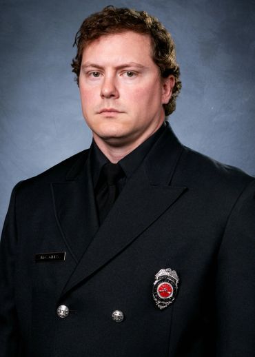 Portrait of a serious firefighter in uniform against a gray background.