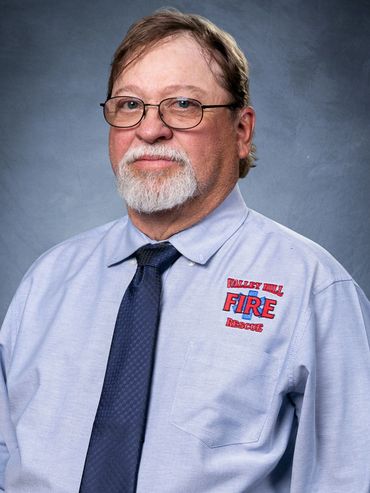 Portrait of a man in a fire rescue uniform shirt with glasses and a beard.