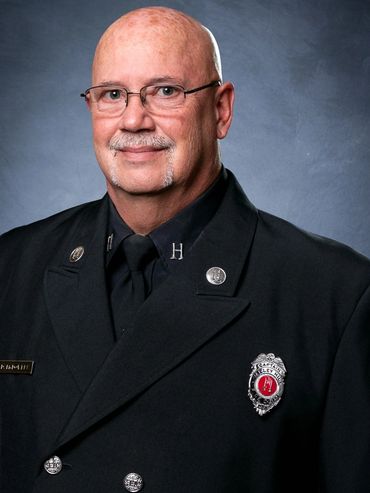 Portrait of a uniformed firefighter with glasses and a mustache.