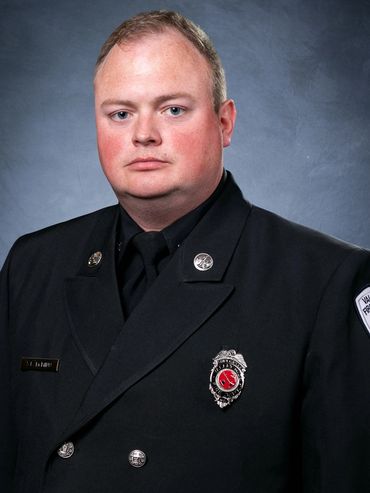 Portrait of a firefighter in formal uniform against a gray backdrop.