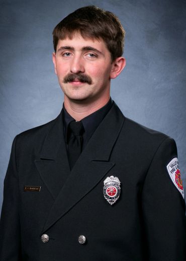 Portrait of a firefighter in formal uniform with badge and nameplate.