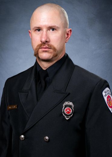 Portrait of a firefighter in formal uniform with badges and a serious expression.
