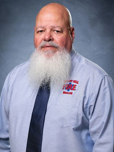 Man with a long white beard wearing a fire rescue shirt and tie.