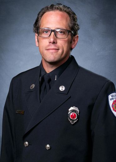 Portrait of a firefighter in formal uniform with badges and glasses.