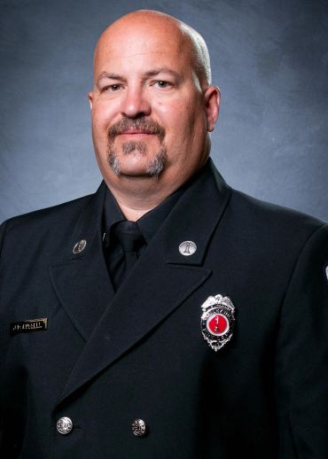 Portrait of a uniformed firefighter with badges and a mustache.