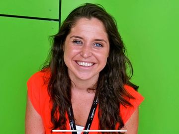 Smiling woman with dark hair in an orange top against a green background.