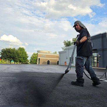 spraying sealer on a parking lot while sealcoating it