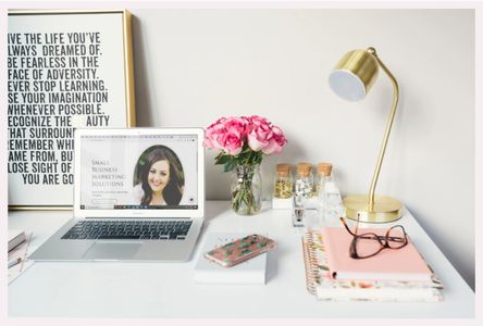 Laptop on white desk with notebooks, gold lamp, and pink roses.