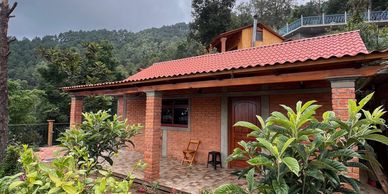 Cozy brick house with a red roof nestled in lush greenery and hills.