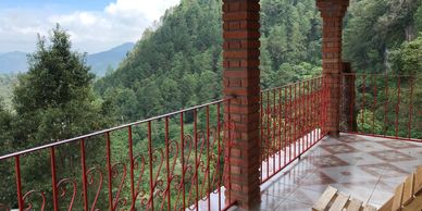 Scenic mountain view from a tiled balcony with red brick columns and railing.