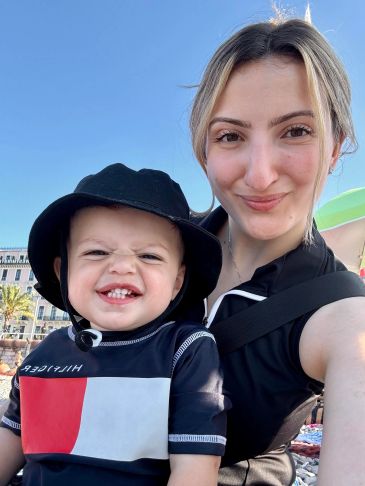 Woman and toddler smiling outdoors in sunny weather.