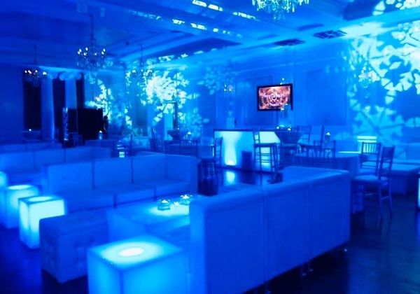 Blue-lit modern lounge with illuminated furniture and decorative wall lights.
