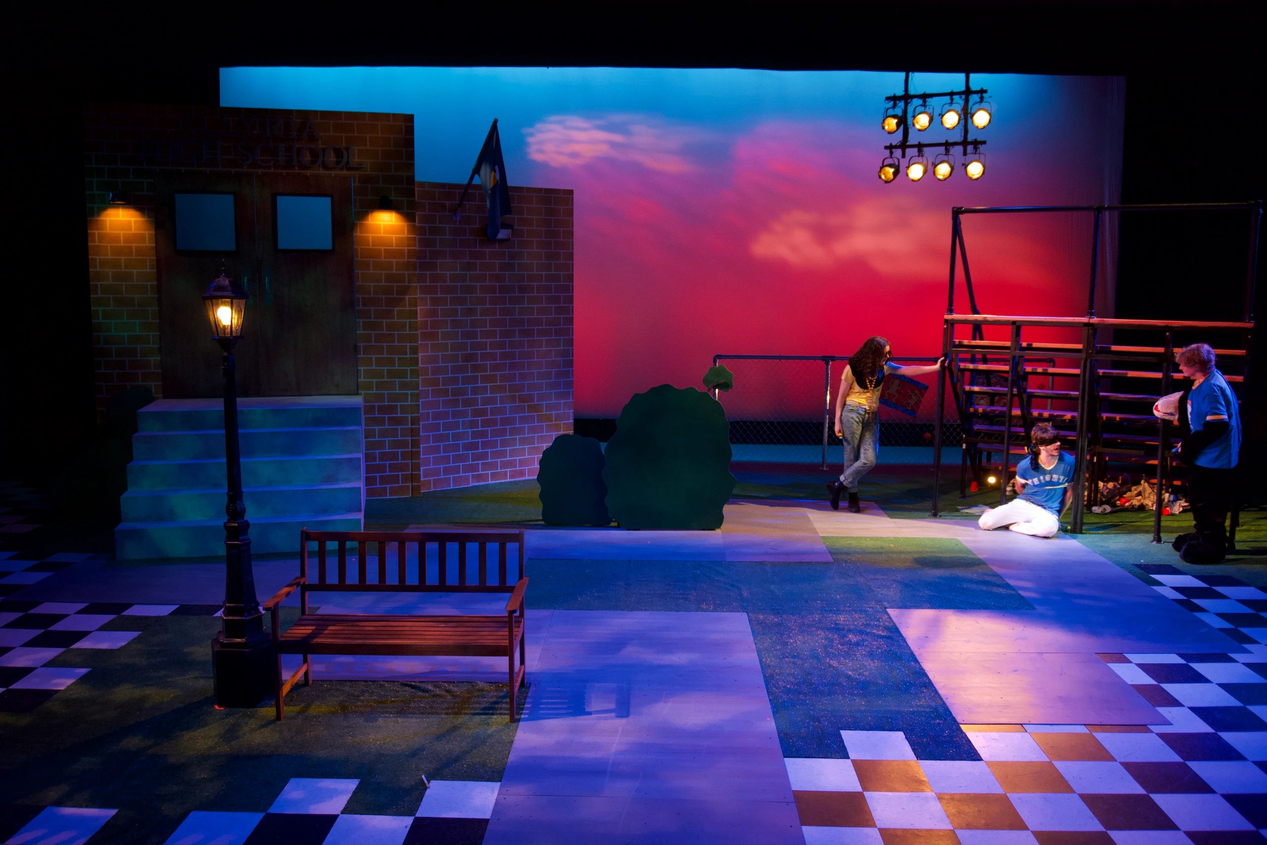 A theatrical high school scene with actors and a sunset backdrop.