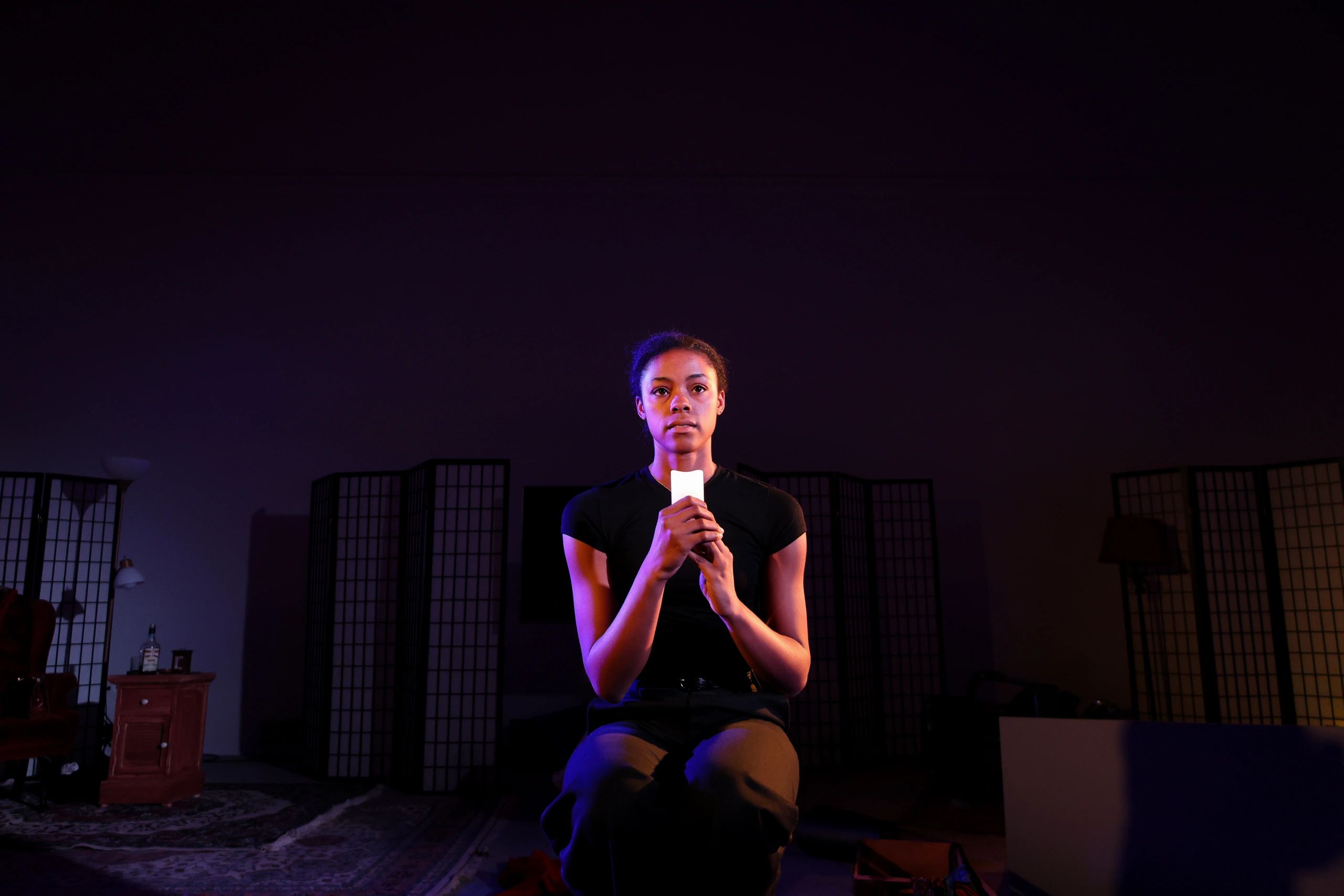 Young woman holding a candle in a dimly lit room with purple lighting.