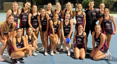 A women's netball team posing together on an outdoor court at night.