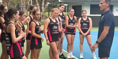 Coach giving instructions to a female sports team on an outdoor court.
