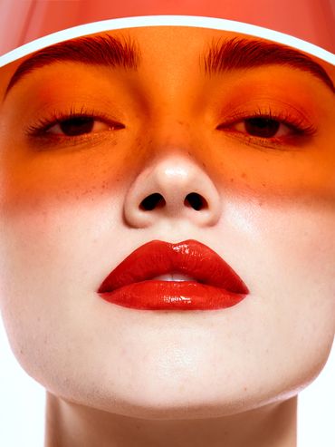 Close-up of a woman with bold red lipstick and an orange translucent visor.