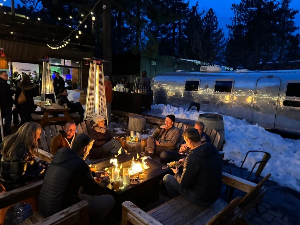 Guests around a fire table on a snowy evening patio under string lights