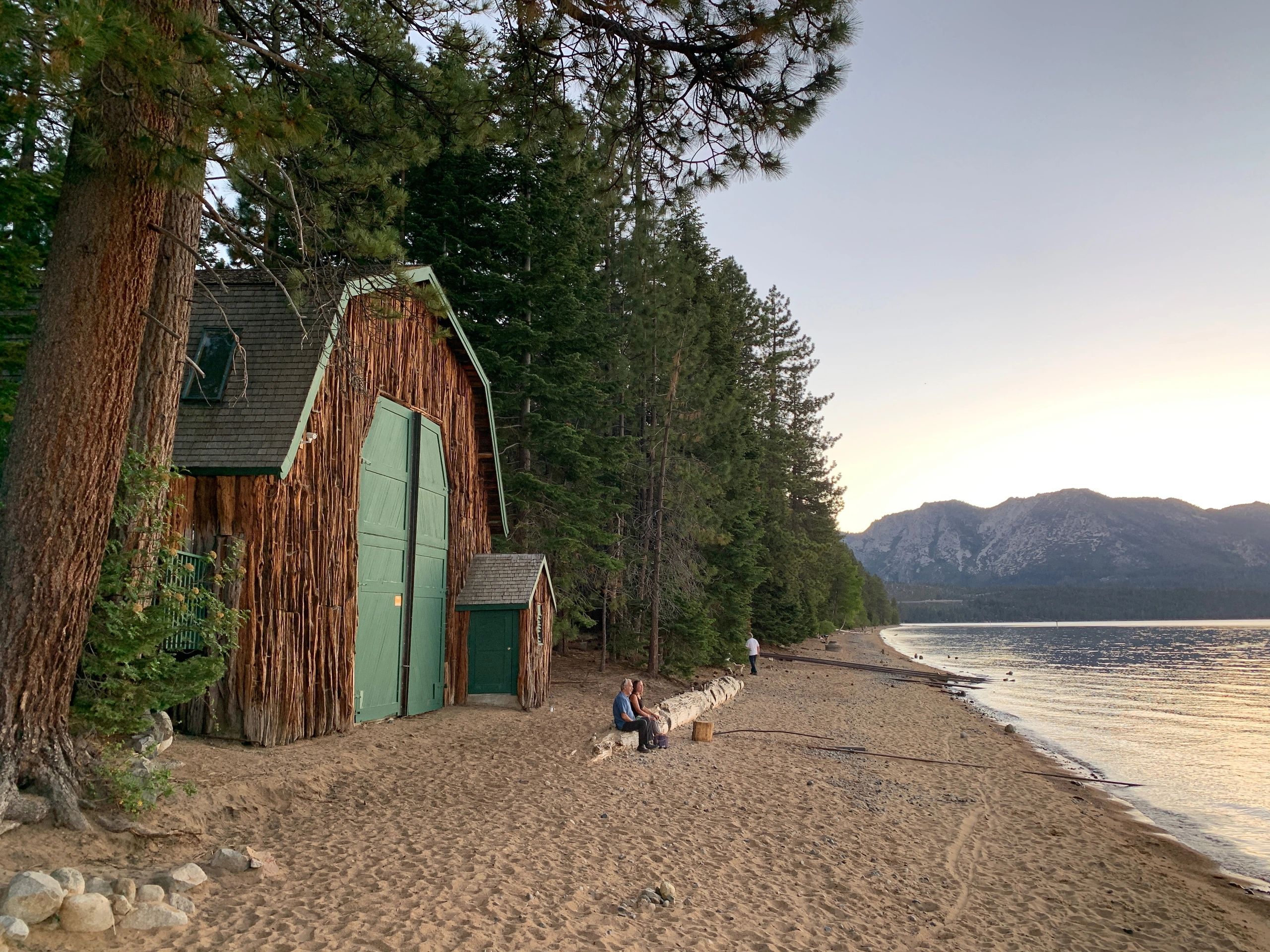 Wooden boathouse on a pine-lined Lake Tahoe beach at sunset