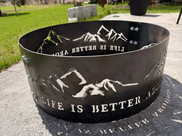 Metal fire pit with mountain design and 'Life is better' inscription.