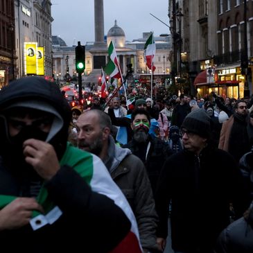 Crowd marching with flags in an urban setting during dusk.