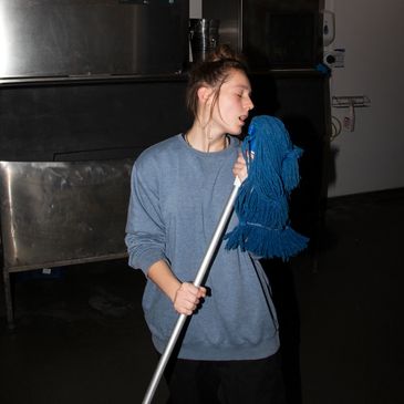 Person singing into a mop handle indoors.