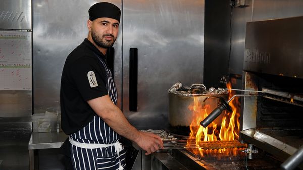 Chef grilling food over an open flame in a professional kitchen.