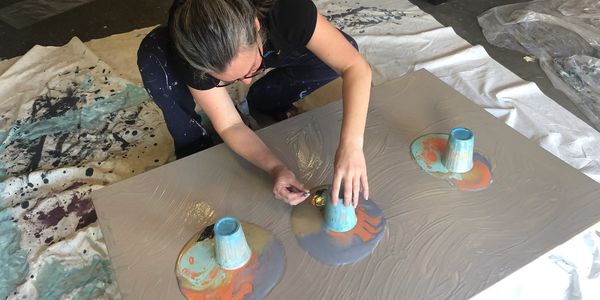 A woman creates art using cups and paint on a canvas.
