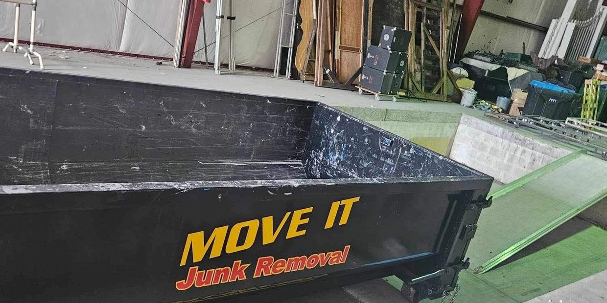 Empty junk removal dumpster inside a warehouse with various stored items.