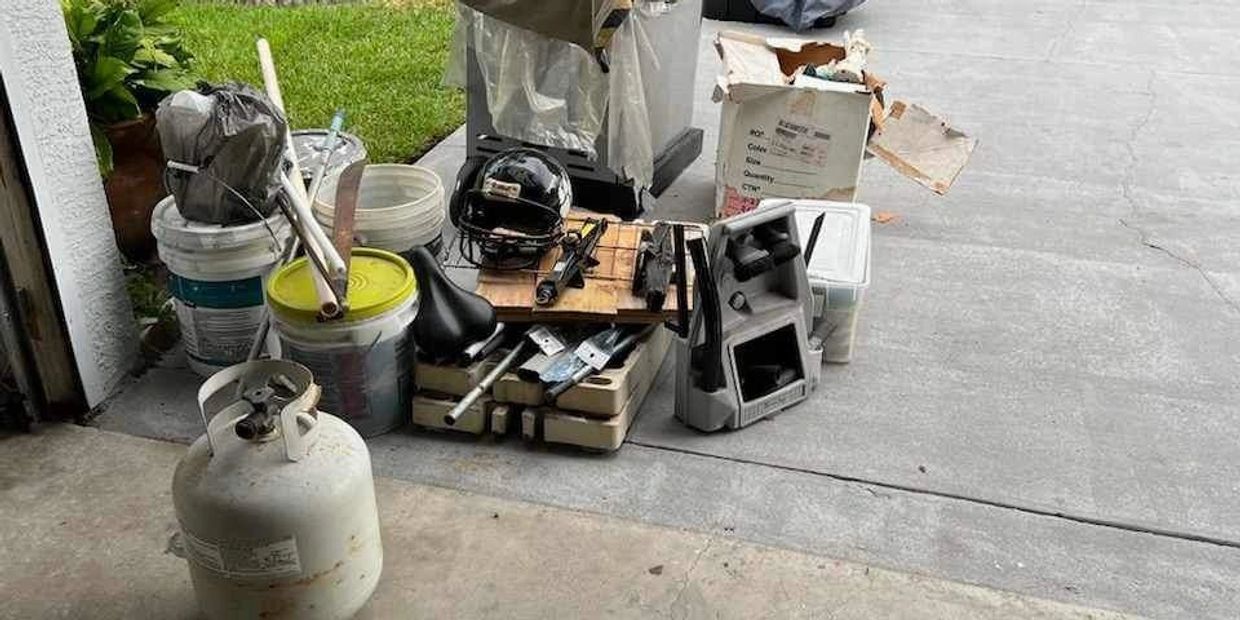 Various household items and tools are placed on a driveway near a garage.