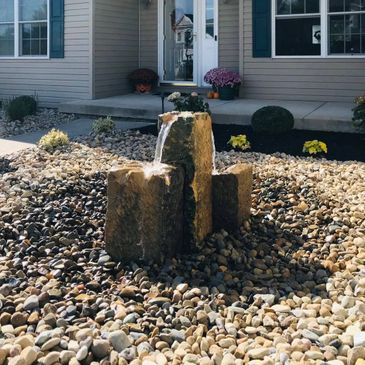 Stone water fountain surrounded by pebbles in front of a house.