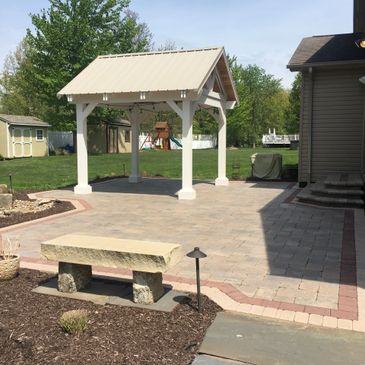Backyard patio with a small pavilion and stone bench under a clear sky.