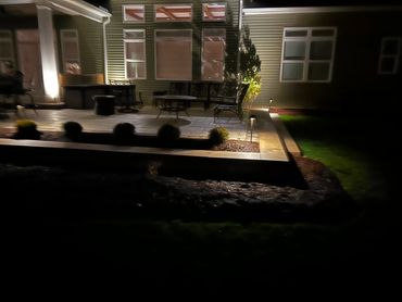 A dimly lit backyard patio area at night with chairs and a table.