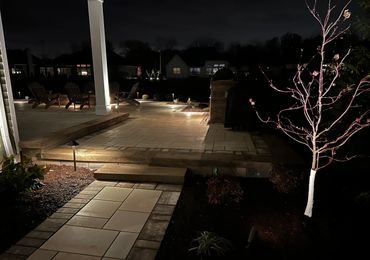 Illuminated outdoor patio and walkway at night with subtle garden lighting.