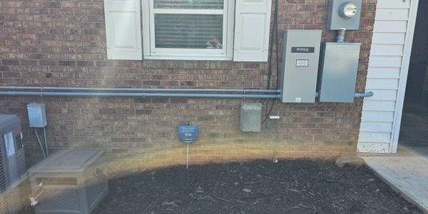 Brick house exterior with utility boxes and mulch bed below a window.
