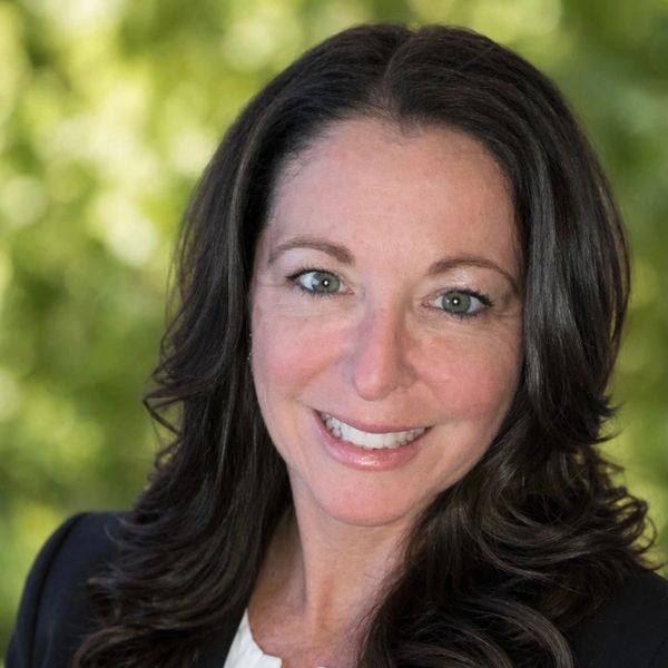 Smiling woman with long dark hair and green eyes in professional attire.