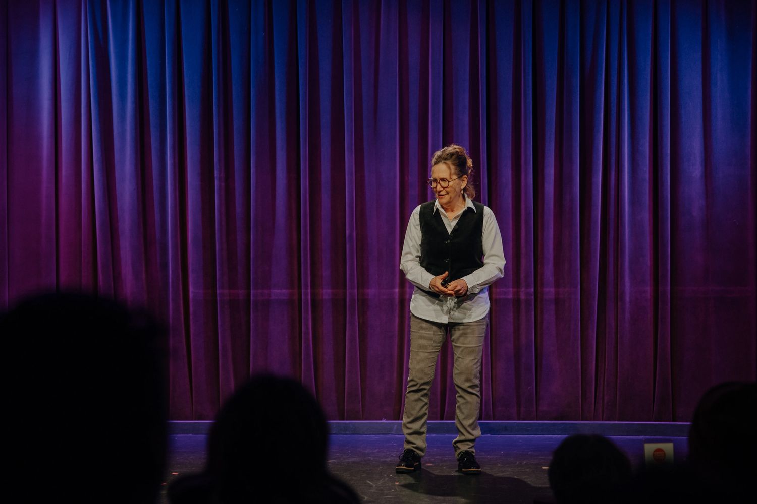 A woman speaks on stage with a purple curtain backdrop.