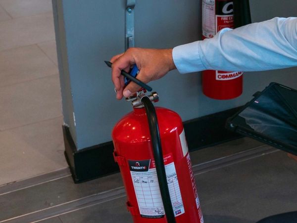 Person inspecting a red fire extinguisher with a pen in hand.